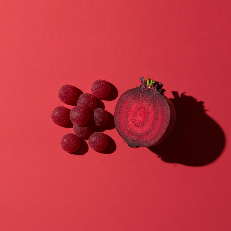 Deep red gummies beside a halved beetroot on a red background