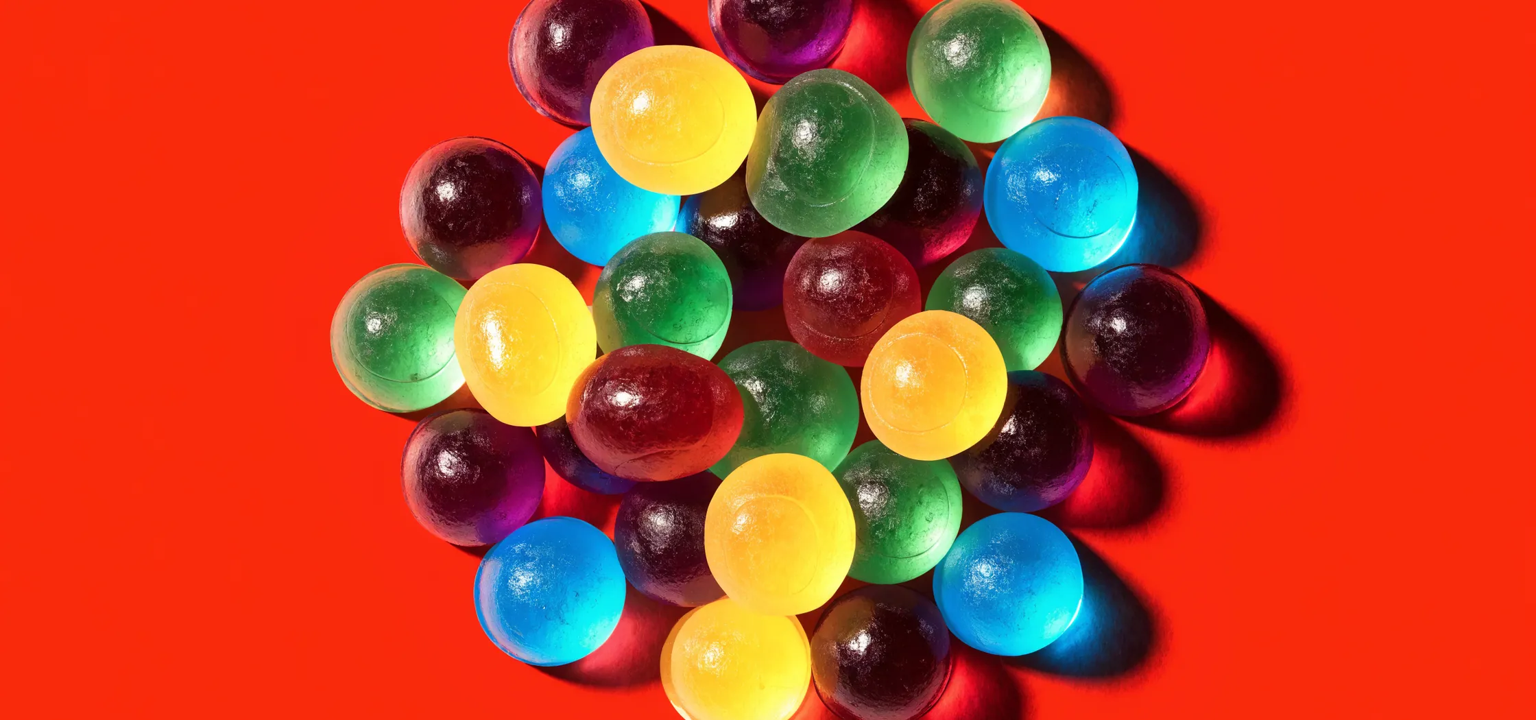 Cluster of purple, yellow, green, red and blue gummy vitamins on an orange background